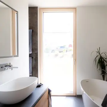 Bodentiefes Panoramafenster im Bad mit Gartenblick und Sonnenuntergang in Fürstenzell. Gefertigt von der Schreinerei Franz Renaltner, Experte für großflächige Fensterlösungen im Raum Passau und München seit 1926.