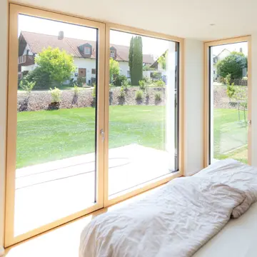 Bodentiefe Panoramafenster und Terrassentür im Schlafzimmer mit Blick auf den Sonnenaufgang. Gefertigt von der Schreinerei Franz Renaltner, Fensterbau-Experte für Passau, Niederbayern und München seit 1926.