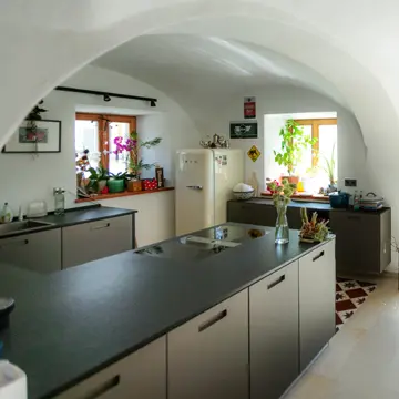 Blick über die Kochinsel auf maßgefertigte Holzfenster und ein doppelflügeliges, bodentiefes Fenster-Türelement im Bauernhaus Fürstenzell-Scheuereck – Fensterhandwerk der Schreinerei Franz Renaltner aus Passau seit 1926.
