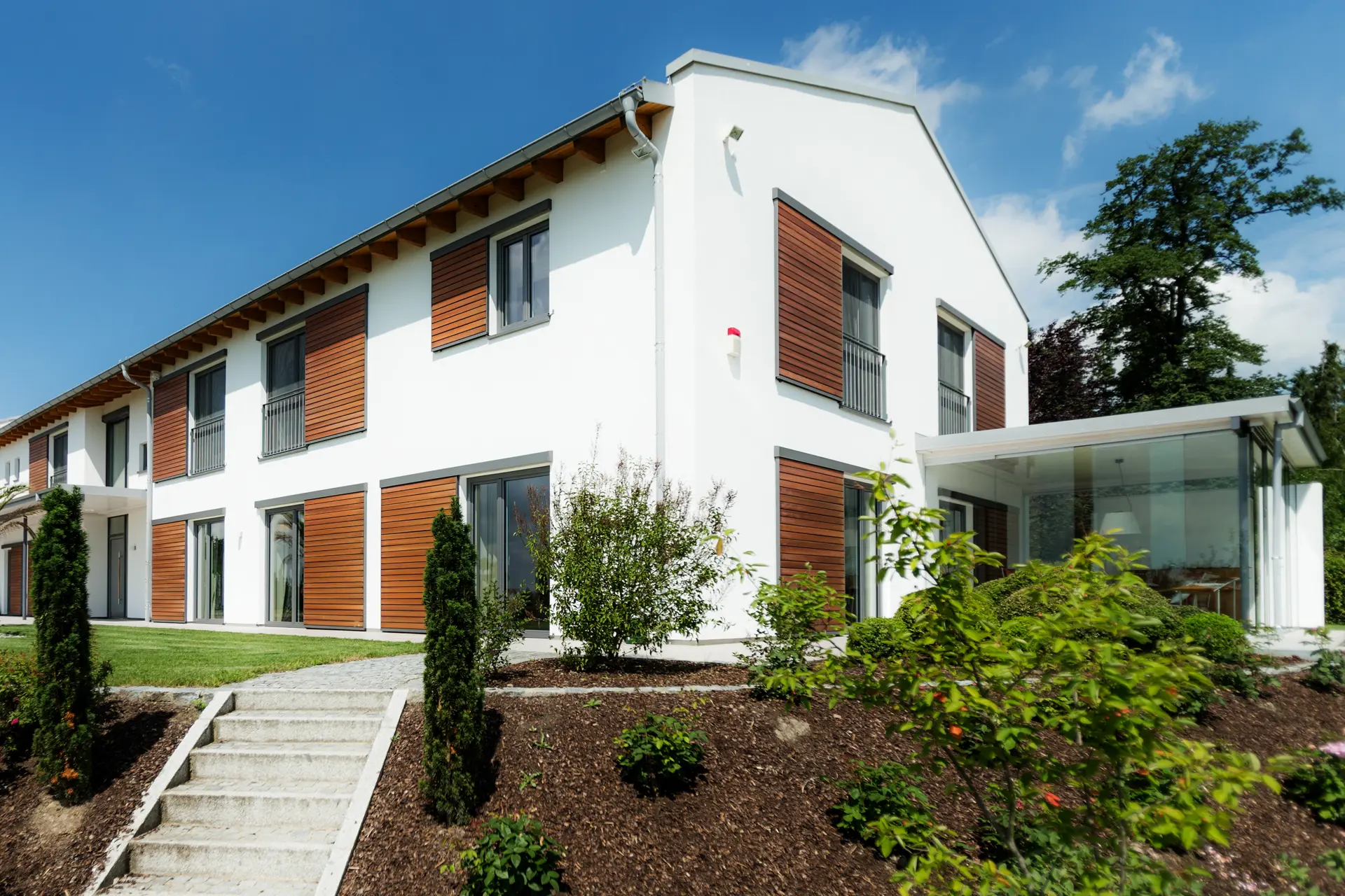 Einbruchshemmende Holz-Alu-Fenster mit integrierter Verschlussüberwachung und Smart-Home-gesteuerten Fensterläden an einer Pfosten-Riegel-Fassade in Vilshofen.
